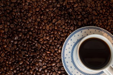 Arka planda bir sürü kahve çekirdeği üzerine siyah kahve fincanı. 