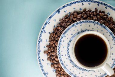 Bir sürü kahve çekirdeği ve mavi arka planda geleneksel bir kahve fincanı.