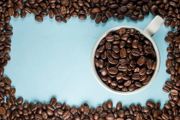 Mavi arka planda geleneksel bir fincanda bir sürü kahve çekirdeği 