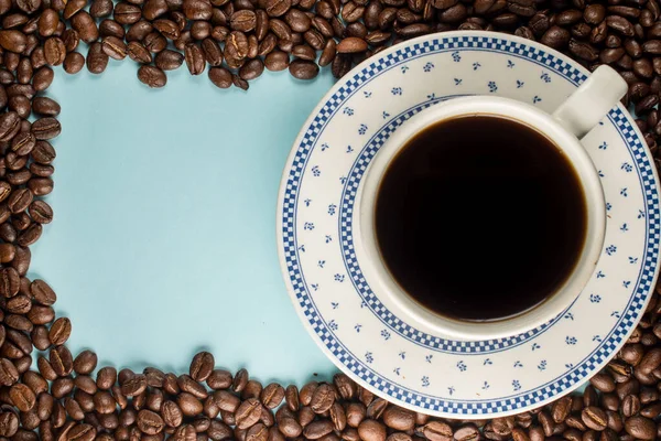 Bir sürü kahve çekirdeği ve mavi arka planda geleneksel bir kahve fincanı.