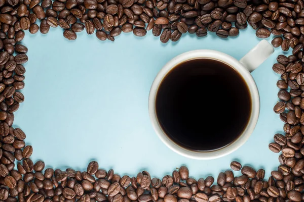 Bir sürü kahve çekirdeği ve mavi arka planda geleneksel bir kahve fincanı.