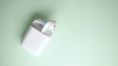 Eller, yeşil arka planda şarj aletlerinde kablosuz kulaklıkları kurtarıyor. 