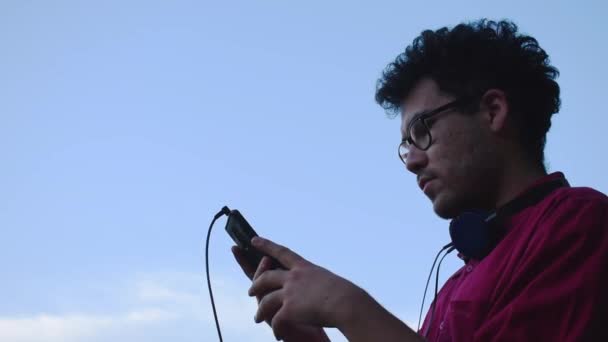 Homme Bouclé Regardant Son Smartphone Puis Mettre Des Écouteurs Sur — Video