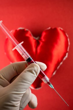 Kan bağışı konusu, doktor eli arka planda kırmızı bir kalbe kan dolu bir şırınga tutuyor.