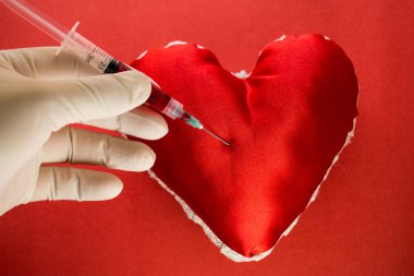 Kan bağışı konusu, doktor eli arka planda kırmızı bir kalbe kan dolu bir şırınga tutuyor.