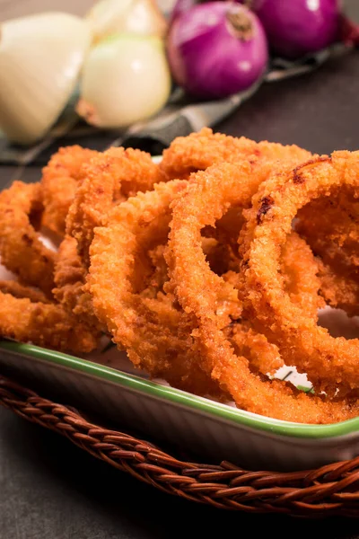 Siyah ahşap bir masada kızarmış soğan halkaları, soğan dilimleri ve mor soğanlar.