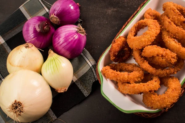 Siyah ahşap bir masada kızarmış soğan halkaları, soğan dilimleri ve mor soğanlar.
