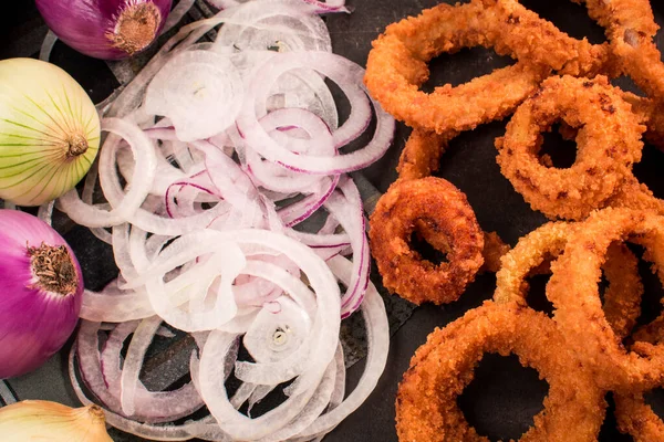 Siyah ahşap bir masada kızarmış soğan halkaları, soğan dilimleri ve mor soğanlar.