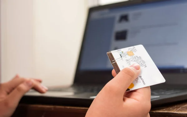 Süveter giyen, kredi kartı tutan ve siyah laptopunu kullanan bir kadın.