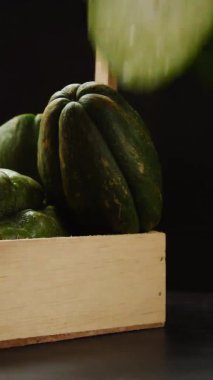 Elin, siyah ahşap masada taze yeşil Latin meyvesi alırken çekilmiş dikey bir video.