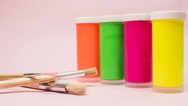  Neon boya, diğer neon boyalar ve pembe arka planda boya fırçaları.