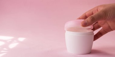 El, pembe arka plandaki kadınlar için bir krem şişesi açıyor.