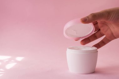 Hand opening a skin cream bottle for women on pink background