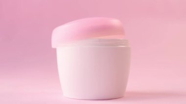 Pembe arka plandaki kadınlar için cilt kremi şişesinden krem almak