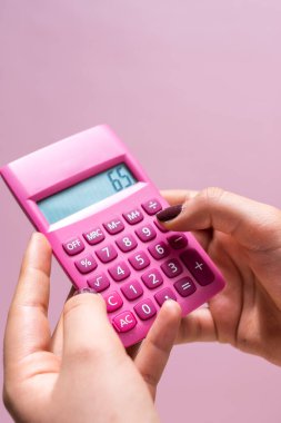 Hands using a pink calculator with white numbers on a pink surface