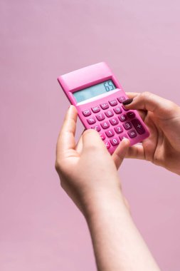 Hands using a pink calculator with white numbers on a pink surface