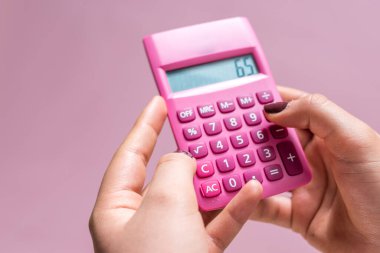 Hands using a pink calculator with white numbers on a pink surface