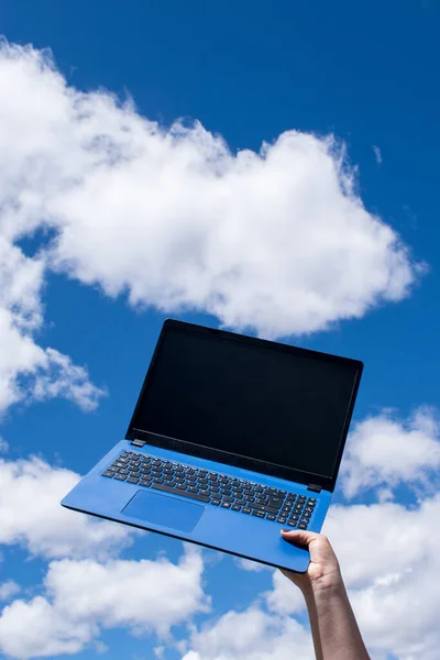 Hand holding a blue laptop and blue sky as background