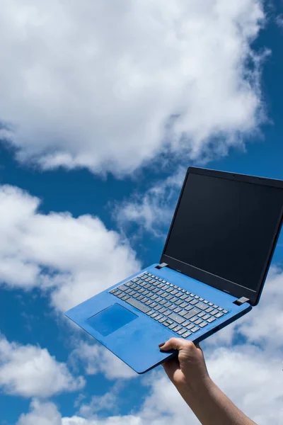 Hand holding a blue laptop and blue sky as background