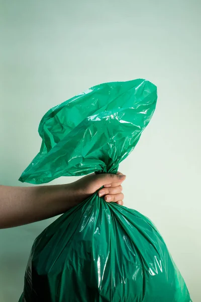 Hand holding a green plastic bag on green background