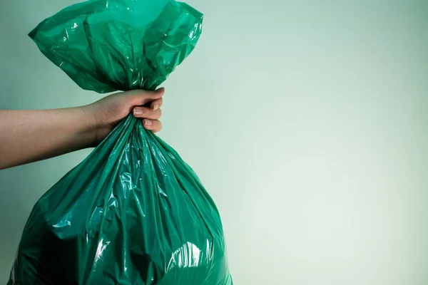 Hand holding a green plastic bag on green background