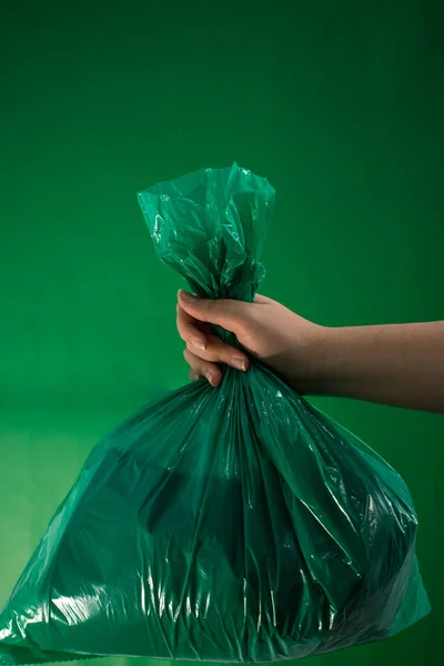 Hand holding a green plastic bag on green background