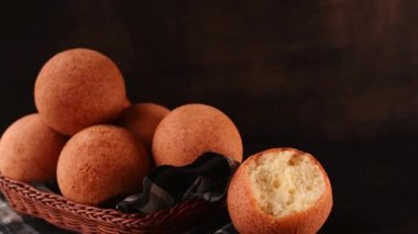 Hand taking a round colombian traditional food named buuelo in a basket on black wooden table