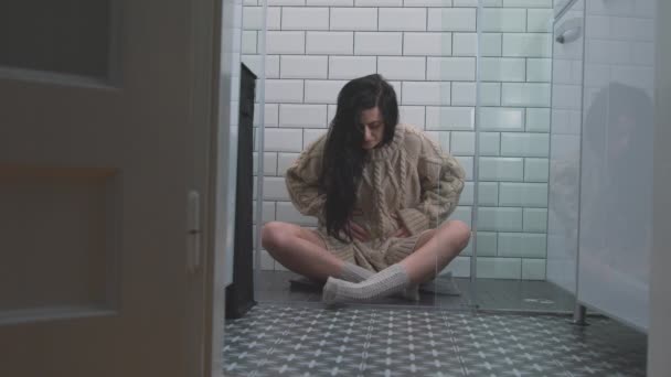 한 소녀 가 바닥에 앉아서 PMS 가 극심 한 통증을 느끼는 가운데 눈살을 찌푸리고 있다 — 비디오