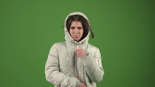 Beautiful girl trying to hide from the wind and cold wearing a jacket on the green background — Stock Video
