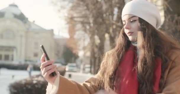 Bastante joven mujer tratando de hablar en video mientras camina a través de una ciudad helada — Vídeo de stock