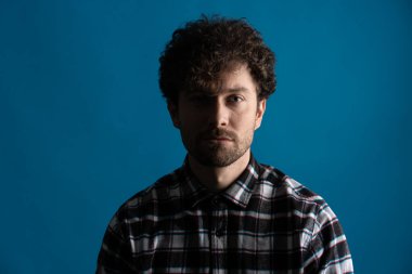 Mavi gözlü ve kameraya poz veren genç, kıvırcık bir adamın çerçevesini kapatın.