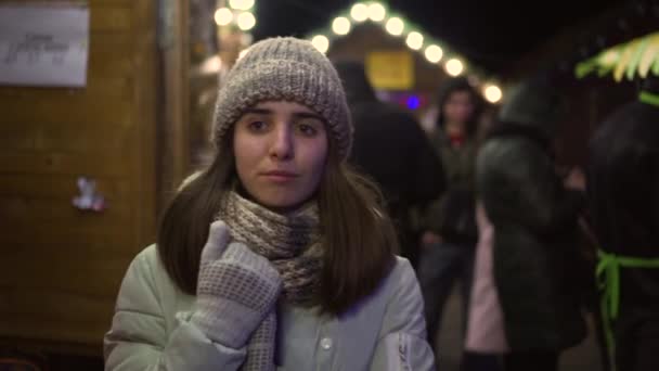Дівчина ходить по новорічній ярмарці і шукає когось знайомого в натовпі. — стокове відео