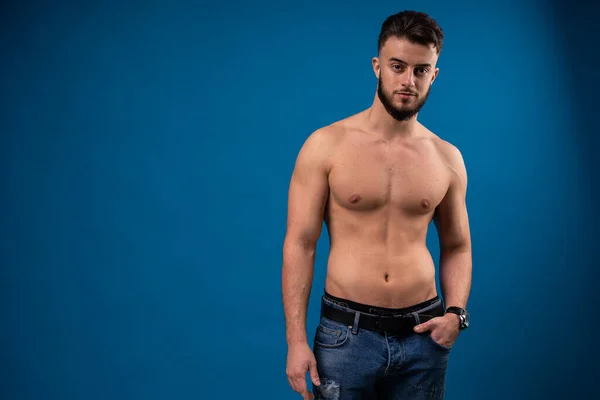 Un tipo guapo con un torso desnudo. Modelo sobre fondo azul mira a la cámara. — Foto de Stock