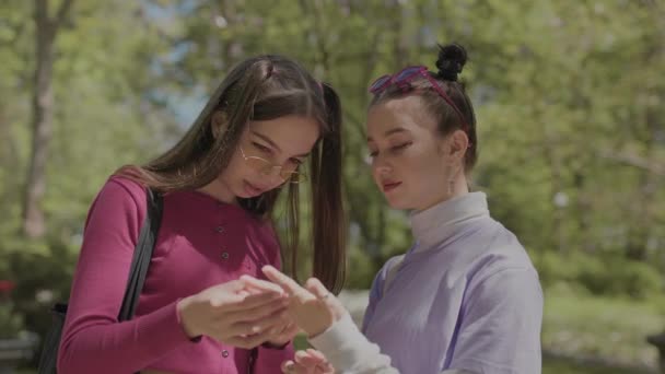 Dziewczyny w jasnych obrazach uwazaja pierscionek na rece. Nastolatki spędzają czas w parku. — Wideo stockowe