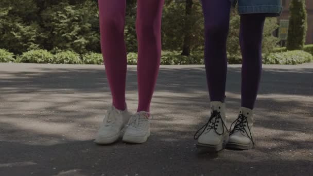 Collant luminosi sulle gambe di ragazze adolescenti sedute su una panchina del parco. — Video Stock