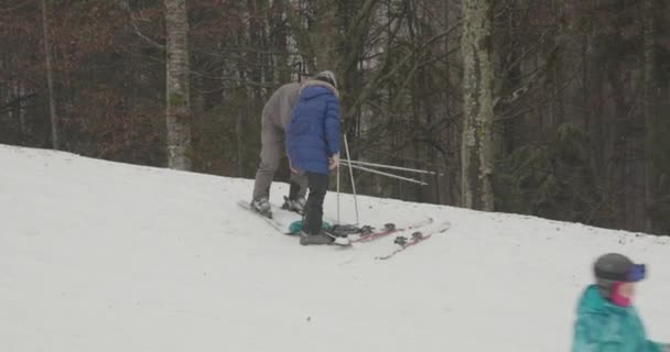 Bukovel, Ukraine - 25. Dezember 2020: Paar schnallt nach Schneefall Ski an — Stockvideo