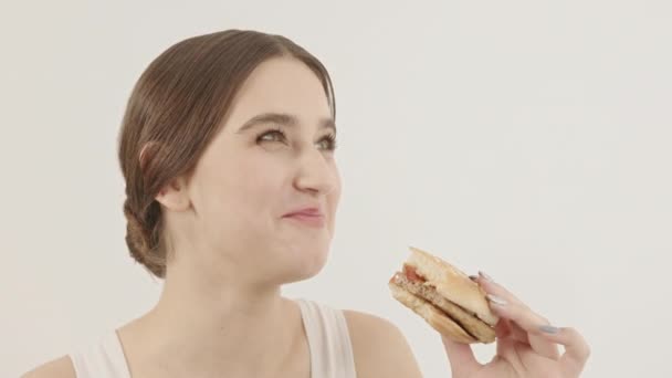 Das Mädchen isst einen Burger und genießt ihn. Genießen Sie das Essen. Kalorienreiche Lebensmittel. — Stockvideo