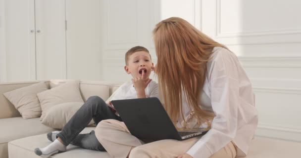 O menino mostra a sua mãe que ele tem uma dor de dente. Mãe e filho em casa sentados no sofá. — Vídeo de Stock