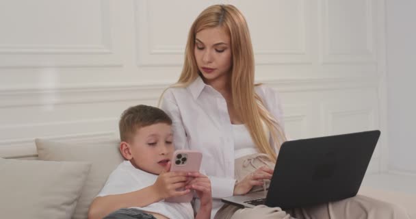 Filho e mãe sentados juntos no sofá em gadgets. — Vídeo de Stock