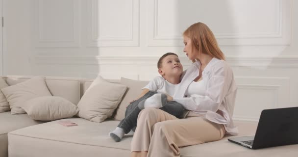 Anya és fia ülnek a kanapén és mosolyogva nézik egymást.. — Stock videók