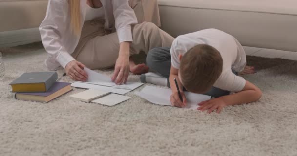 De zoon schrijft een ansichtkaart en de moeder maakt een papieren vliegtuig. Papierproducten met eigen handen. — Stockvideo