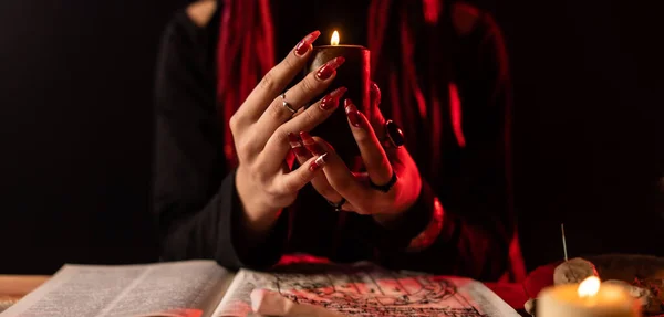 En häxa som utför en ritual med ett ljus. Ljusa i kvinnliga händer med röda långa naglar. — Stockfoto