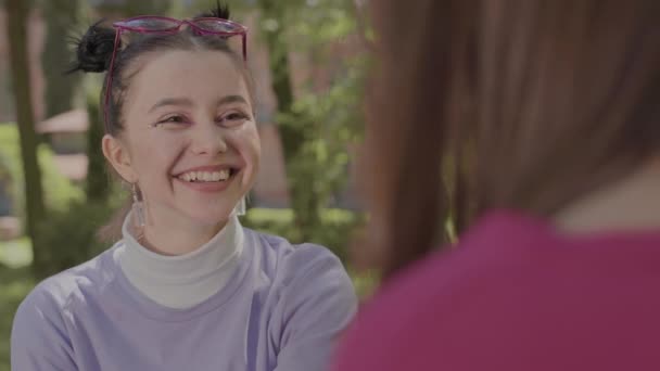 Girls blowing bubbles from chewing gum. Girls play with chewing gum on a park bench. — Stock Video