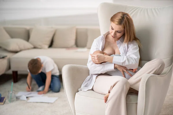 Mam geeft borstvoeding aan een baby die op een stoel zit. Moeder in weeën. — Stockfoto