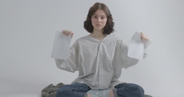 Meisje scheurt een vel papier op een witte achtergrond zittend op de grond. Belediging van collega 's. — Stockvideo