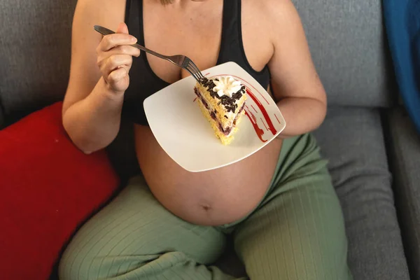 Un pedazo de pastel en un plato en las manos de una mujer embarazada. En una mano un pastel, en la otra un tenedor. —  Fotos de Stock