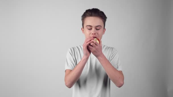 A fiú étvágygerjesztően eszik egy almát, élvezi az édes ízét. — Stock videók