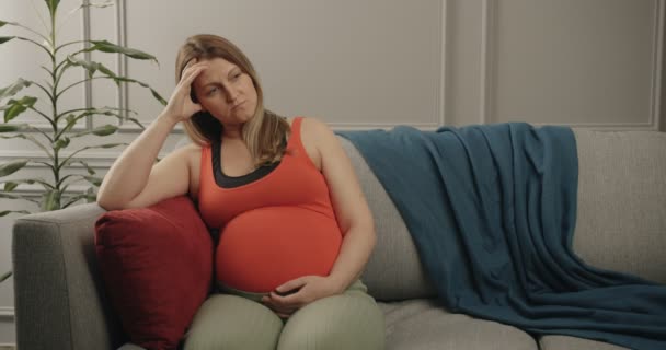 A terhes nő csendben pihen otthon egy nehéz nap után. Terhes nő ül kanapén a szobában. — Stock videók