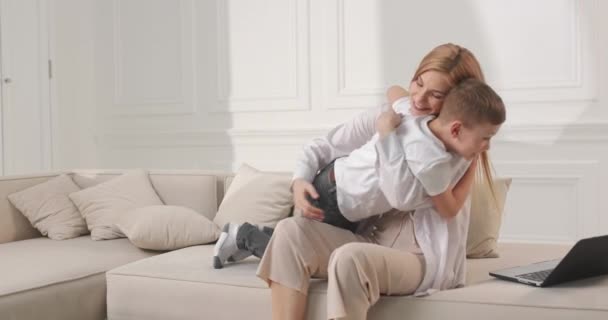 Anya megöleli a fiát a kanapén ülve. Az anyai szeretet a legerősebb a világon.. — Stock videók