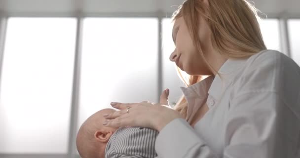 La madre sostiene al bebé en sus brazos y acaricia la cabeza del bebé. — Vídeos de Stock
